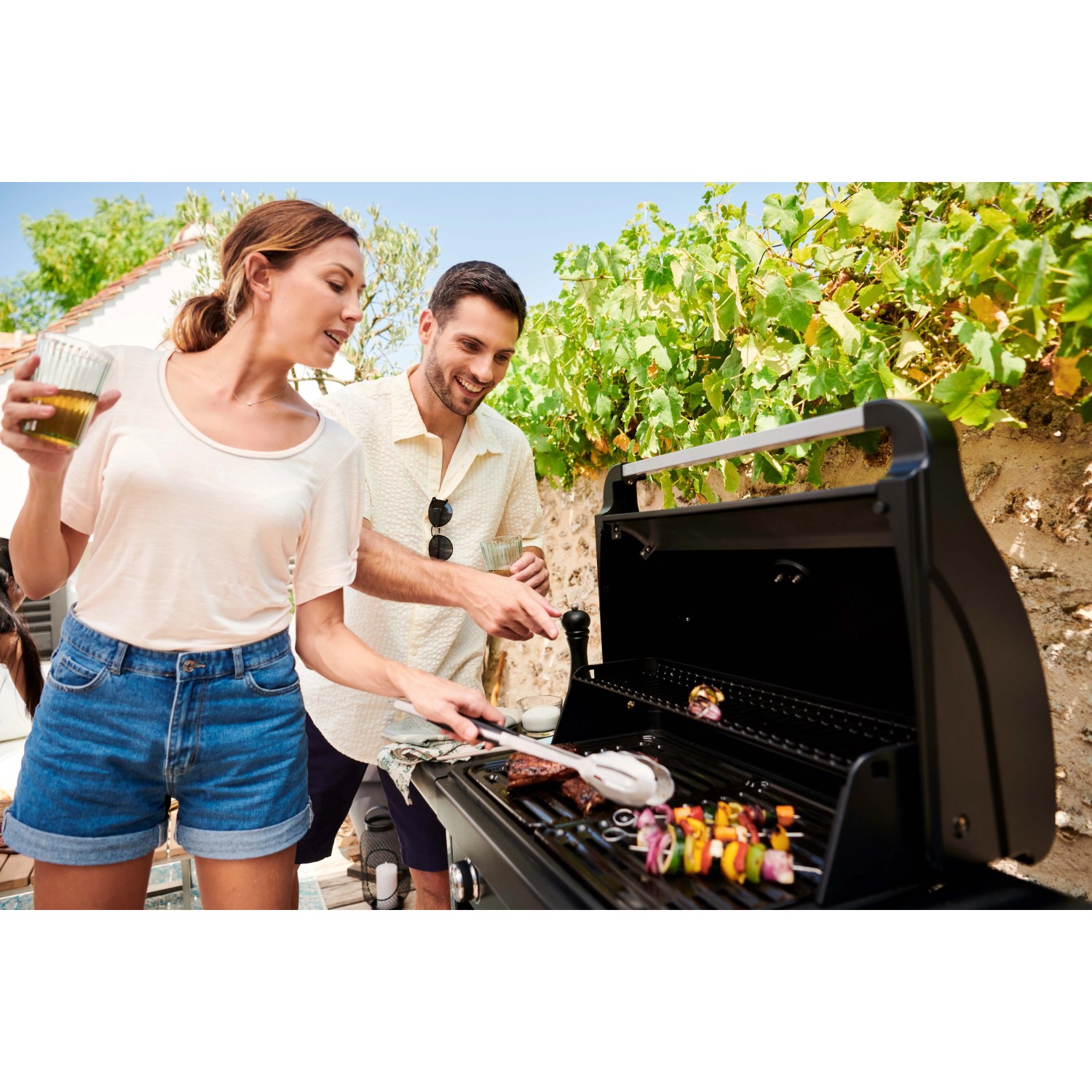 Coppia che griglia con barbecue a gas t.b.t. in giardino. Carne e verdure grigliate sulla griglia.