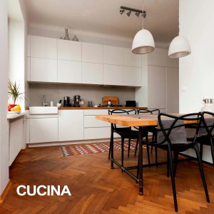 Cucina luminosa con mobili bianchi, tavolo in legno e sedie nere.