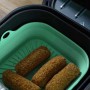 Friggitrice ad aria con contenitore in silicone verde e crocchette. Contenitore per una facile pulizia.