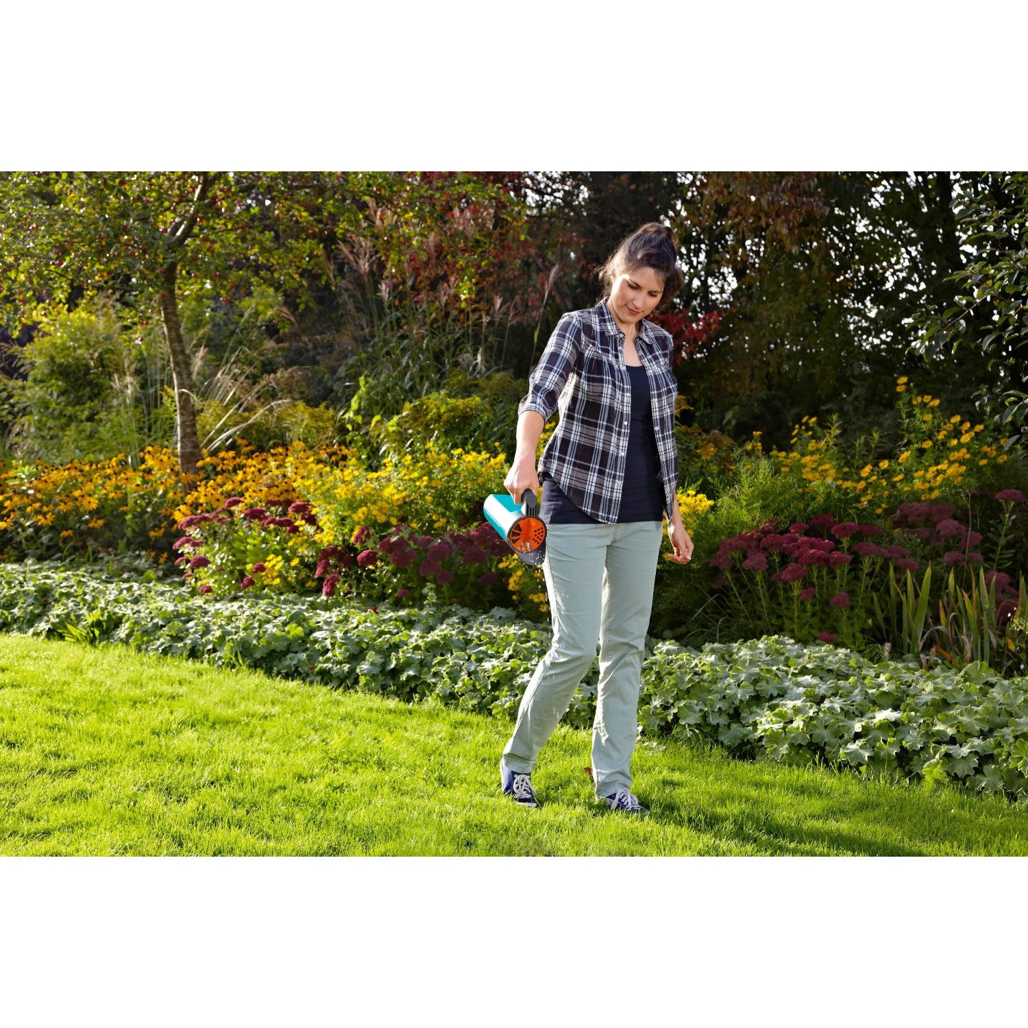 Donna che utilizza lo spargitore manuale Gardena Kleinstreuer S turchese in giardino per fertilizzare.