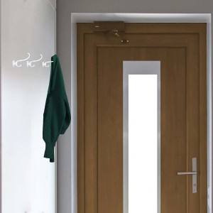 Maglione verde appeso a appendiabiti da parete bianco davanti a una porta di legno.