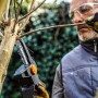 Uomo taglia ramo con motosega a una mano Worx Nitro WG325E. Motosega a batteria compatta in uso.