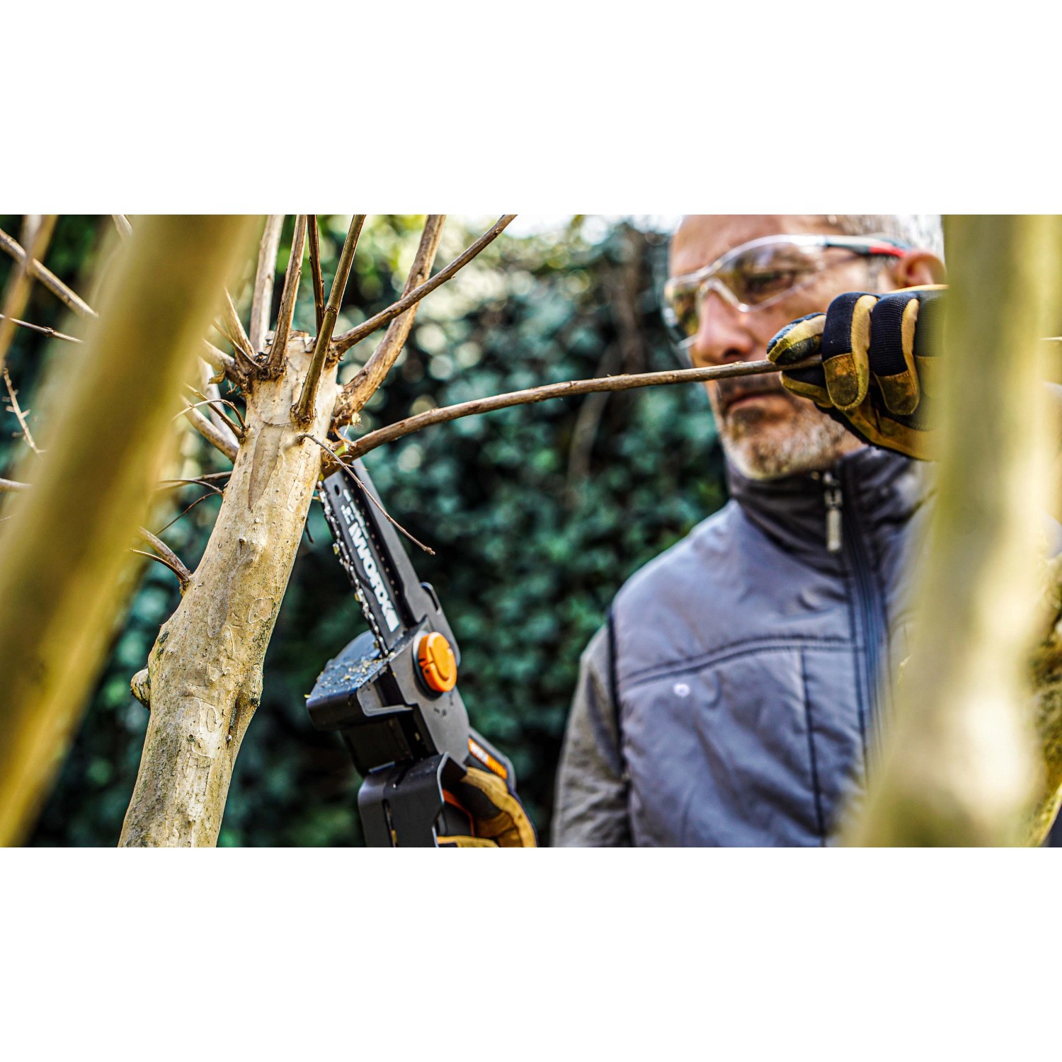 Uomo taglia ramo con motosega a una mano Worx Nitro WG325E. Motosega a batteria compatta in uso.