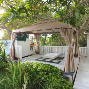 Gazebo beige con tende e lettino su una terrazza in giardino.