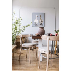 Sala da pranzo con tavolo in legno, sedie con cuscini e dipinto di oche sulla parete.