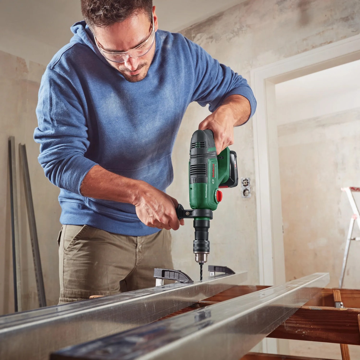 Uomo che fora un profilo metallico con trapano a percussione a batteria Bosch UniversalHammer 18V.