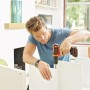 Uomo che assembla mobili con avvitatore a batteria Black+Decker. Avvitatore con batteria e custodia.