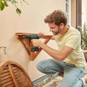 Uomo con occhiali di sicurezza usa avvitatore a batteria Bosch 18V EasyImpact 18V-40 per montare mensola in legno.