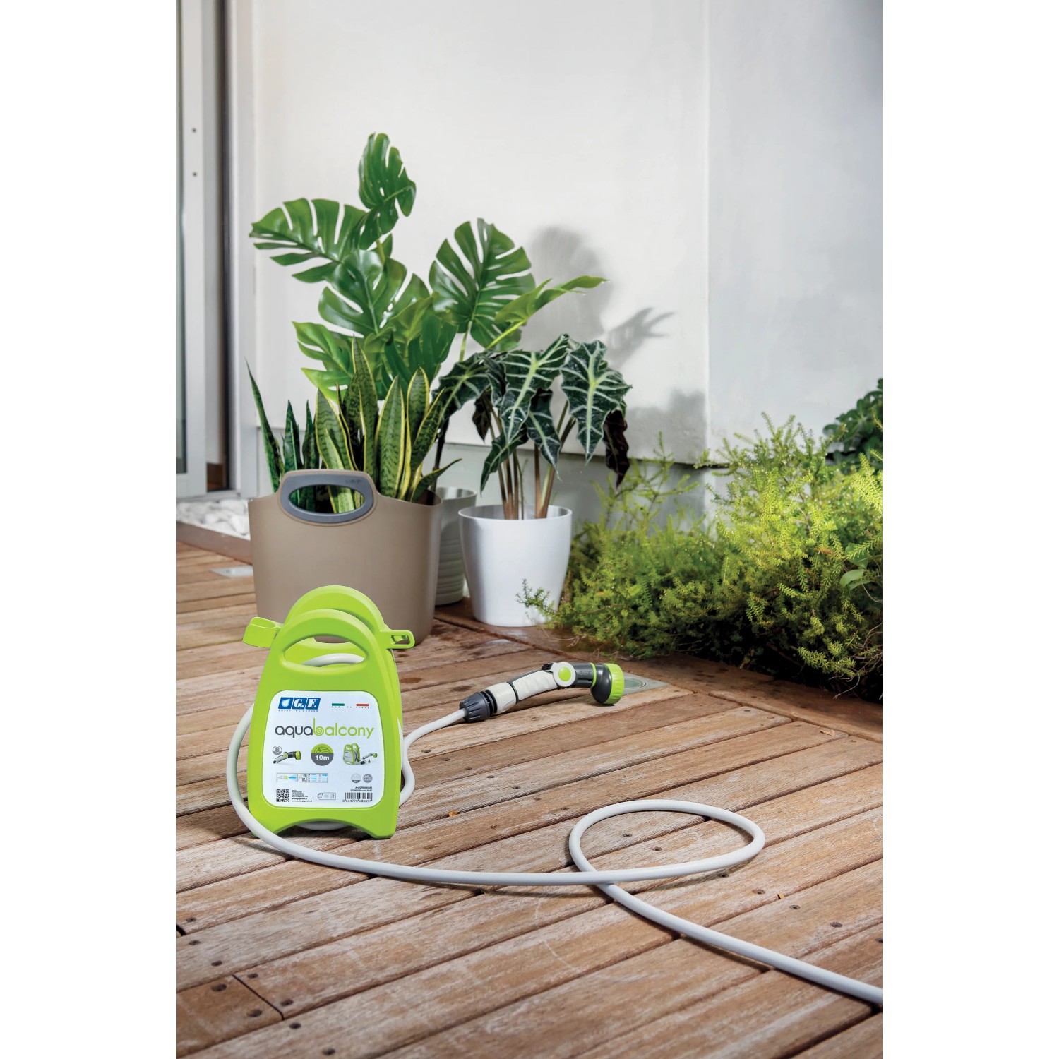 Unità di irrigazione t.b.t. verde e portatile con tubo e testina a spruzzo su terrazza in legno.