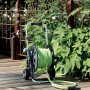 Avvolgitubo nero con tubo da giardino verde su patio in legno.