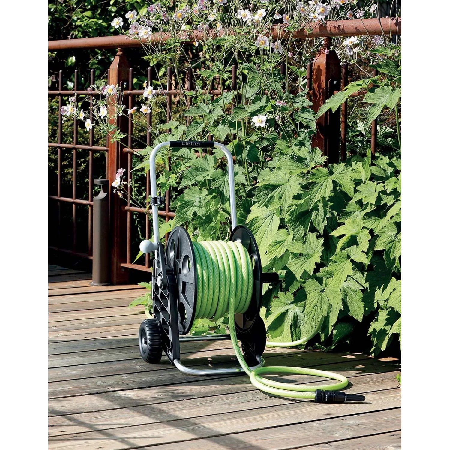 Avvolgitubo nero con tubo da giardino verde su patio in legno.