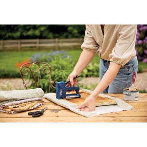 Scena con sparachiodi blu che fissa il tessuto a una cornice di legno su un tavolo all'aperto.