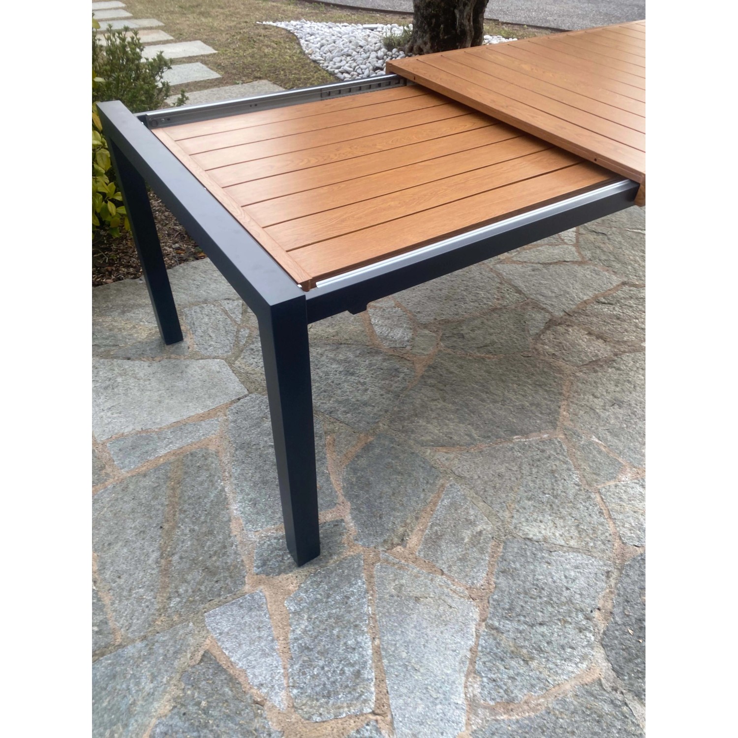 Tavolo da giardino allungabile con piano effetto legno e struttura in metallo scuro.