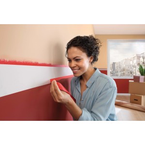 Donna applica nastro adesivo rosso t.b.t. alla parete per dipingere.