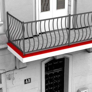 Battiscopa rosso su un balcone con ringhiera grigia.