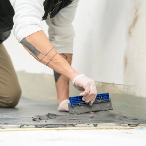 Artigiano che applica adesivo per piastrelle Mapei C2TE sul pavimento.