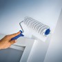 Rullo a dispersione LUX 18 cm mentre dipinge una parete, rullo per pittura con pelo corto a righe grigie.