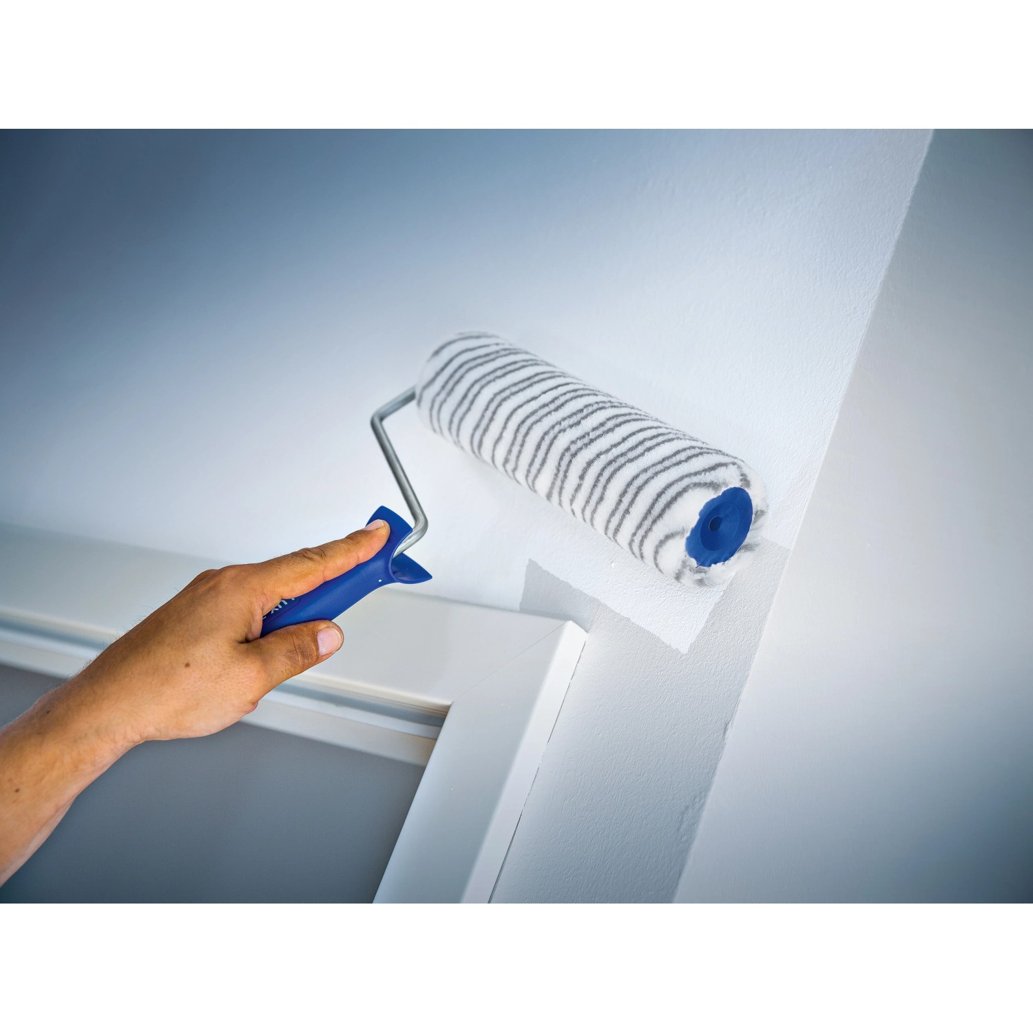 Rullo a dispersione LUX 18 cm mentre dipinge una parete, rullo per pittura con pelo corto a righe grigie.