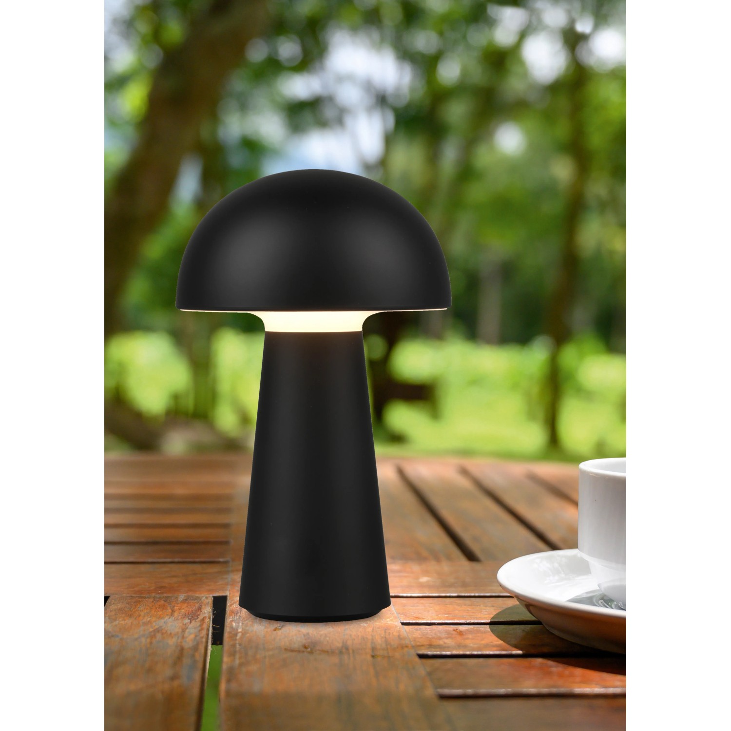 Lampada da tavolo LED Reality Lennon nera a forma di fungo, Ø 13,6 cm, su tavolo di legno in giardino.