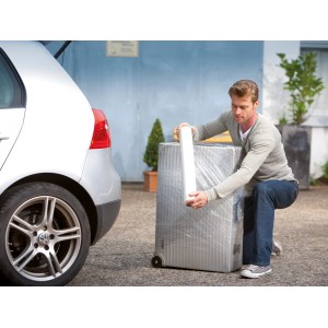 Uomo che avvolge una valigia con pellicola estensibile LUX (0,5 m x 120 m) davanti a un'auto. Materiale di copertura per trasloco.