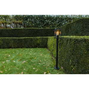 Lanterna da giardino t.b.t. nera su prato davanti a siepe verde.