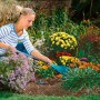 Donna che fa giardinaggio con manico di prolunga per piccoli attrezzi Gardena combisystem 78 cm e rastrello.