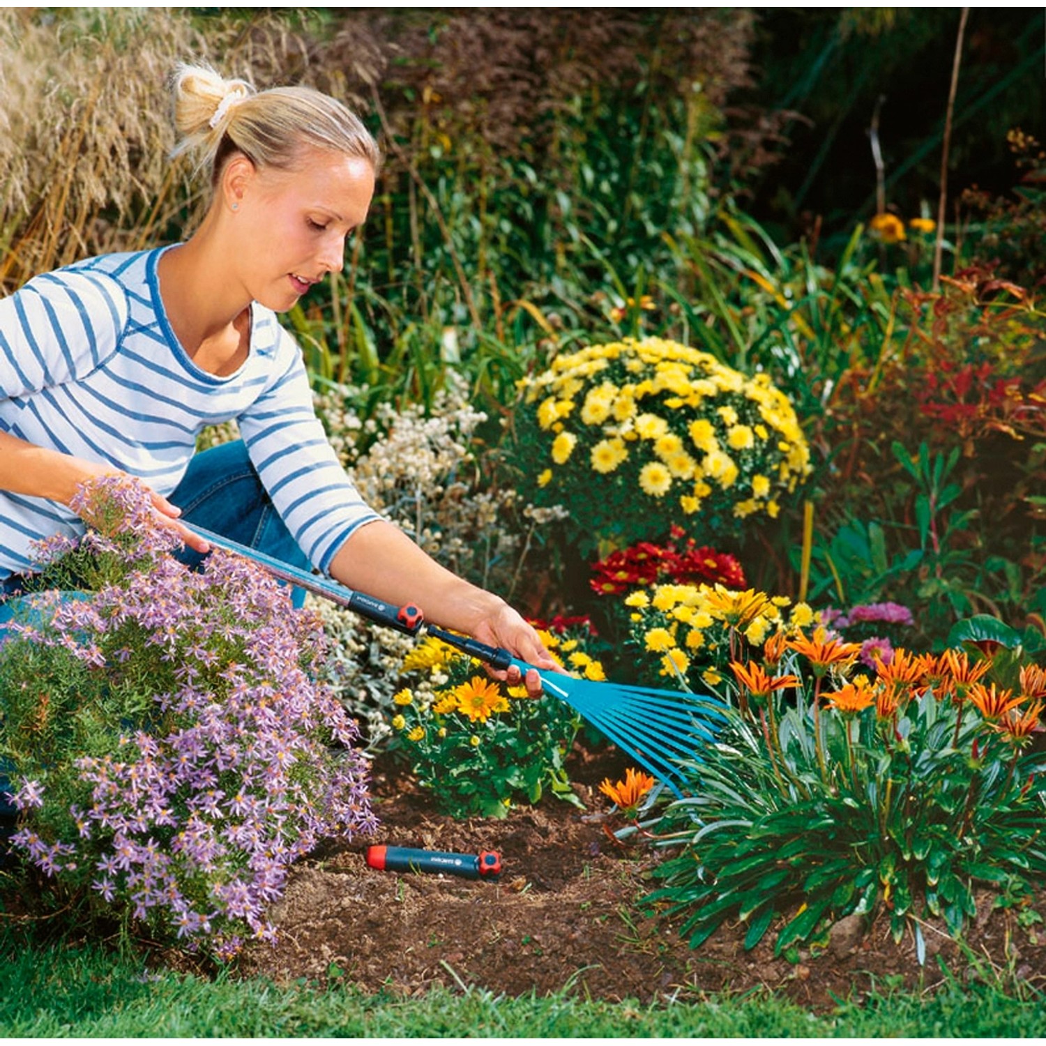Donna che fa giardinaggio con manico di prolunga per piccoli attrezzi Gardena combisystem 78 cm e rastrello.