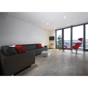 Soggiorno con piastrelle per pavimenti t.b.t. grigie effetto legno, divano e poltrona rossa.