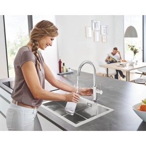 Donna riempie bicchiere con miscelatore cucina Grohe Blue Home cromato, bocca alta.