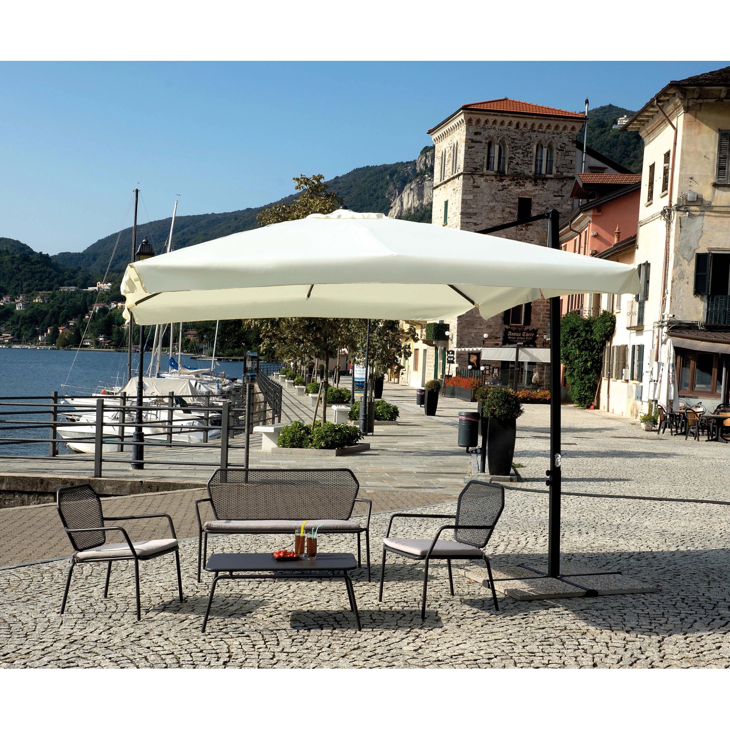 Ombrellone a braccio t.b.t. sopra area salotto con tavolo in piazza.