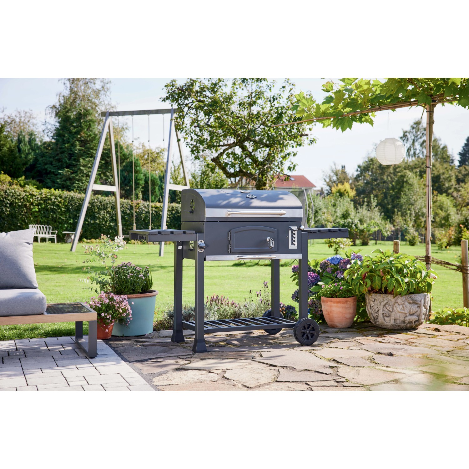 Barbecue a carbonella t.b.t. in giardino con piante e altalena.