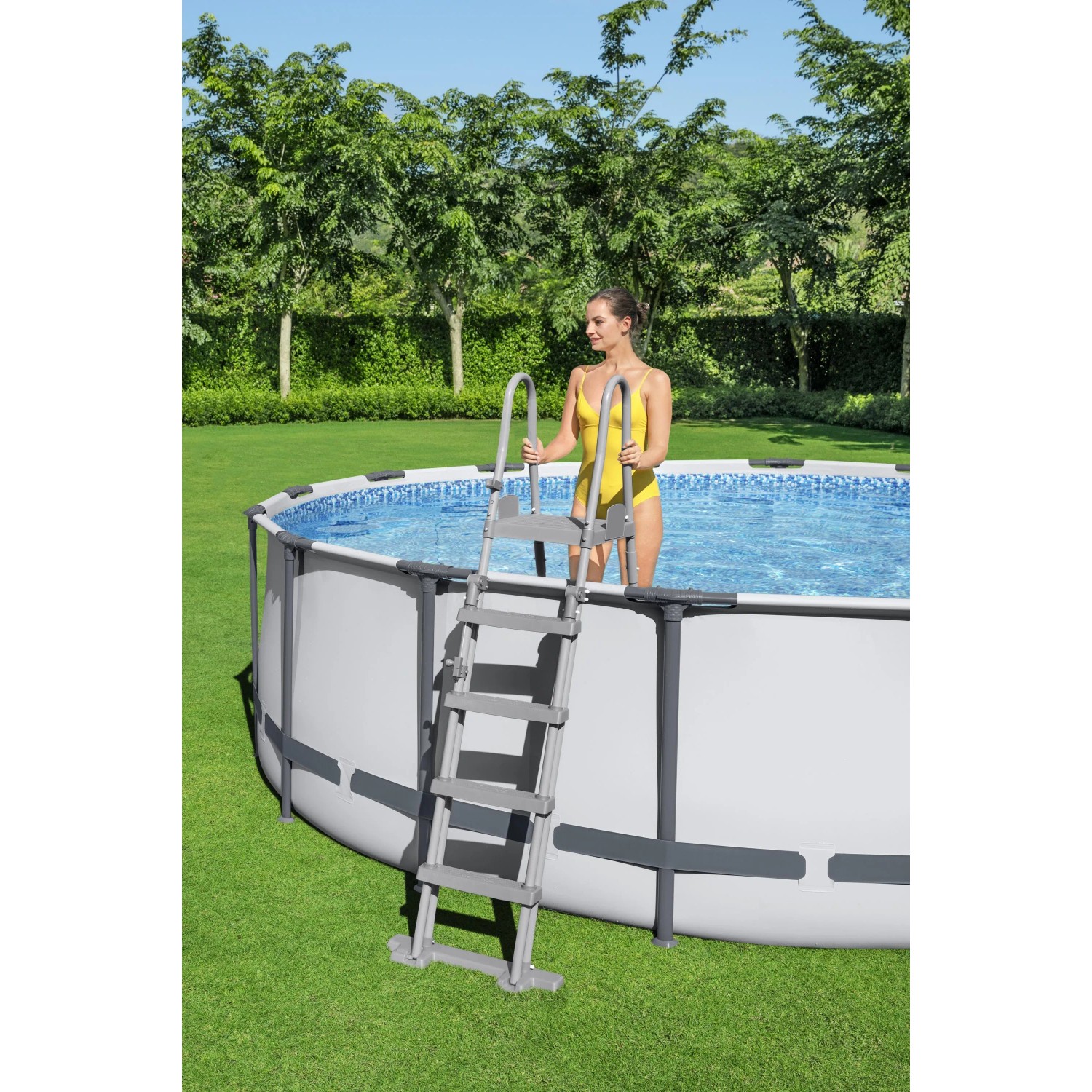 Scala grigia per piscina su piscina fuori terra con donna in costume giallo. Scalette per piscina.