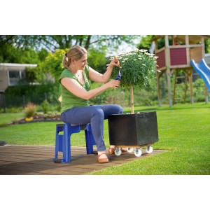 Donna seduta su sgabello da giardino LUX blu con ginocchiera, pota pianta in giardino.