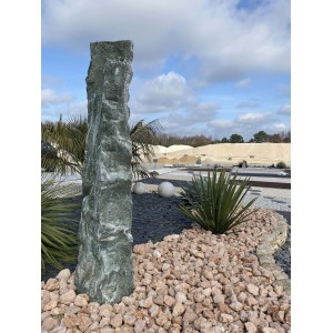 Stele decorativa in Ciottoli e Granulati circondata da ghiaia e piante.