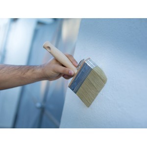 Mano che tiene un pennello LUX 10x3 cm mentre dipinge un muro. Lavori di pittura con pennello di alta qualità.