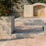 Giardino con elementi di muro e scale in pietra, bordura e fontana sullo sfondo.