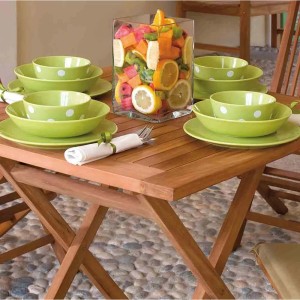 Tavolo da giardino in legno con stoviglie verdi e decorazione di frutta.