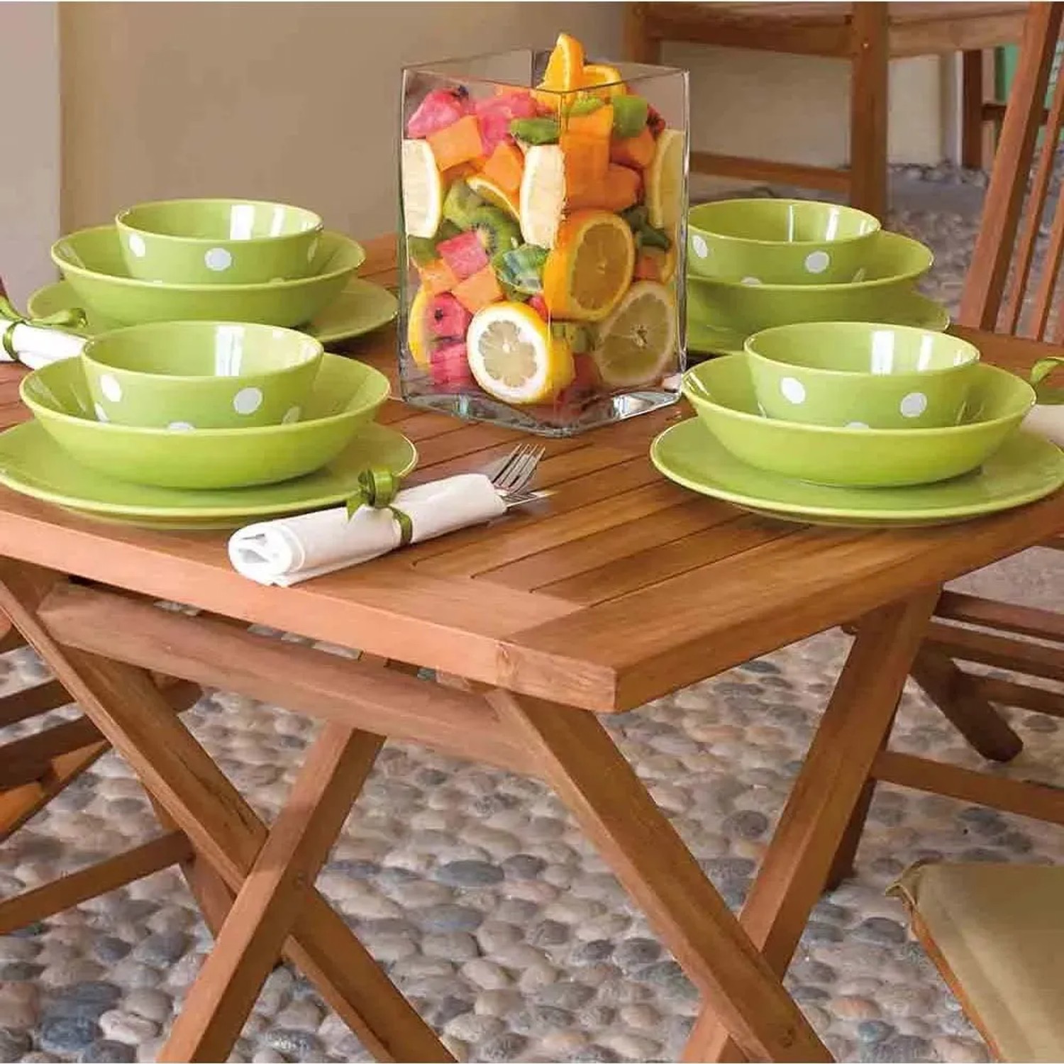 Tavolo da giardino in legno con stoviglie verdi e decorazione di frutta.