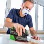 Uomo che leviga il legno con levigatrice multifunzione a batteria LUX A-MS-20. Maschera antipolvere e contenitore per la polvere per un lavoro pulito.