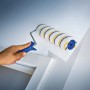 Rullo a dispersione LUX 18cm mentre dipinge una parete. Rullo per pittura con rivestimento in polymix, a righe oro-grigio.