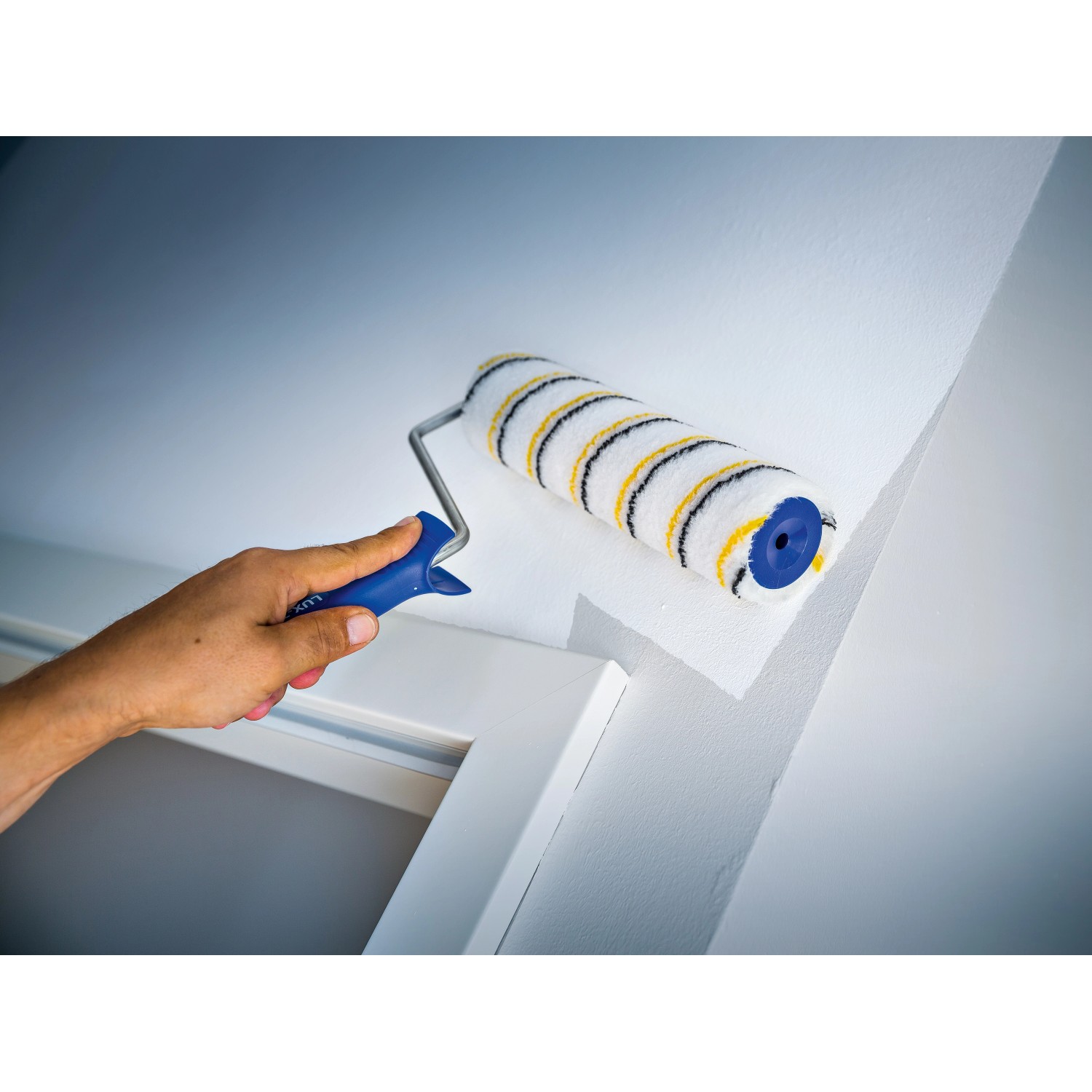 Rullo a dispersione LUX 18cm mentre dipinge una parete. Rullo per pittura con rivestimento in polymix, a righe oro-grigio.