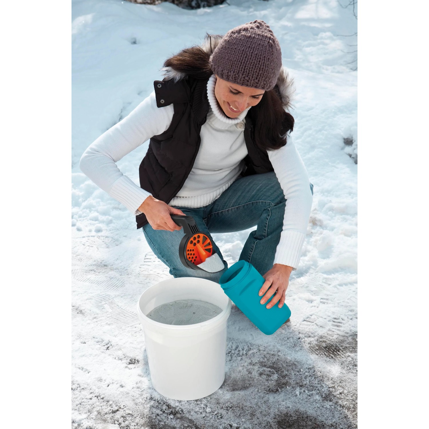 Donna riempie lo spargitore Gardena Kleinstreuer S (turchese) con materiale antighiaccio da un secchio. Spargitore per servizi invernali.