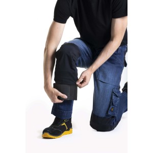 Uomo inginocchiato con abbigliamento da lavoro t.b.t. e ginocchiere. Pantaloni da lavoro blu con rinforzi neri.