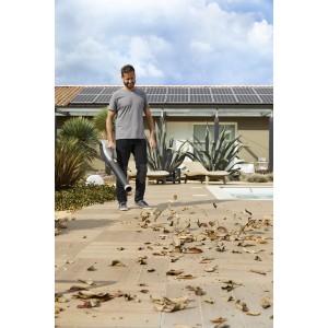 Uomo che usa un aspirafoglie/soffiatore a batteria per rimuovere le foglie in giardino.