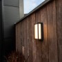 Moderna lampada da parete per esterni a LED Lutec Qubo color antracite con luce bianca calda su parete in legno.