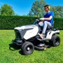 Trattorino tagliaerba mentre taglia l'erba in giardino. Il trattore è bianco e grigio.