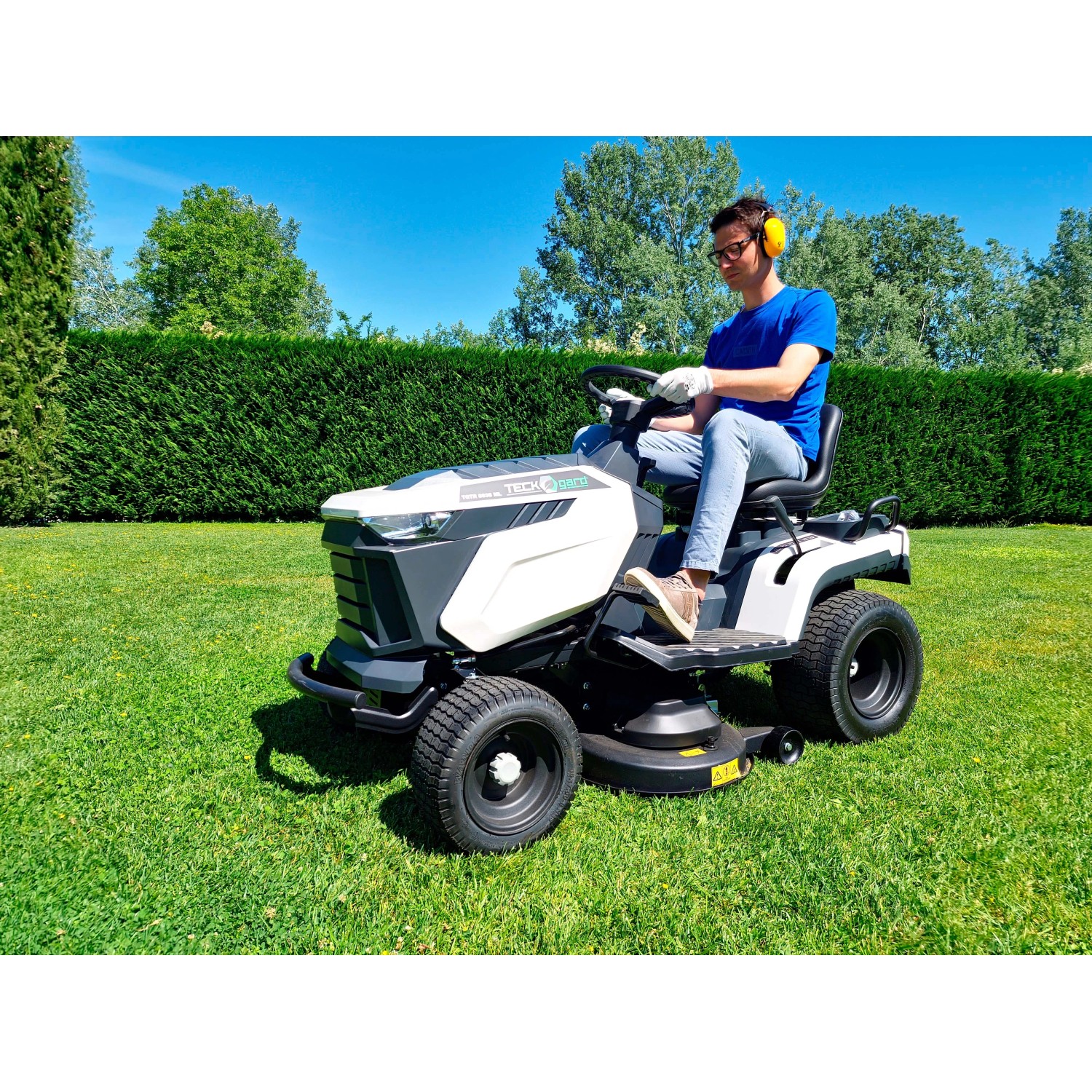 Trattorino tagliaerba mentre taglia l'erba in giardino. Il trattore è bianco e grigio.