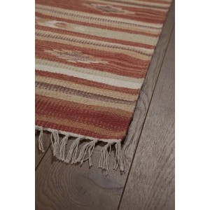 Tappeto t.b.t. con motivo a righe nei toni del rosso e del beige su pavimento in legno.
