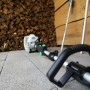 Decespugliatore/tagliabordi, appoggiato su pavimento in pietra, catasta di legna sullo sfondo.