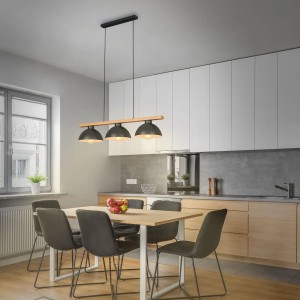 Lampada a sospensione nera t.b.t. con tre paralumi sopra un tavolo da pranzo in cucina.
